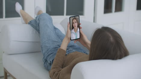 Young-female-Sick-at-Home-Using-Smartphone-to-Talk-to-Her-Doctor-via-Video-Conference-Medical-App.-Woman-Has-Conversation-with-Professional-Physician-Using-Online-Video-Chat-Application.